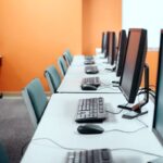 Fila de computadores de escritorio en una sala de cómputo empresarial moderna y bien iluminada, listos para uso corporativo
