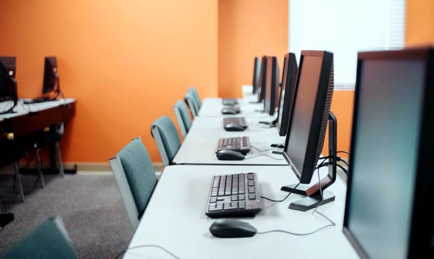 Fila de computadores de escritorio en una sala de cómputo empresarial moderna y bien iluminada, listos para uso corporativo