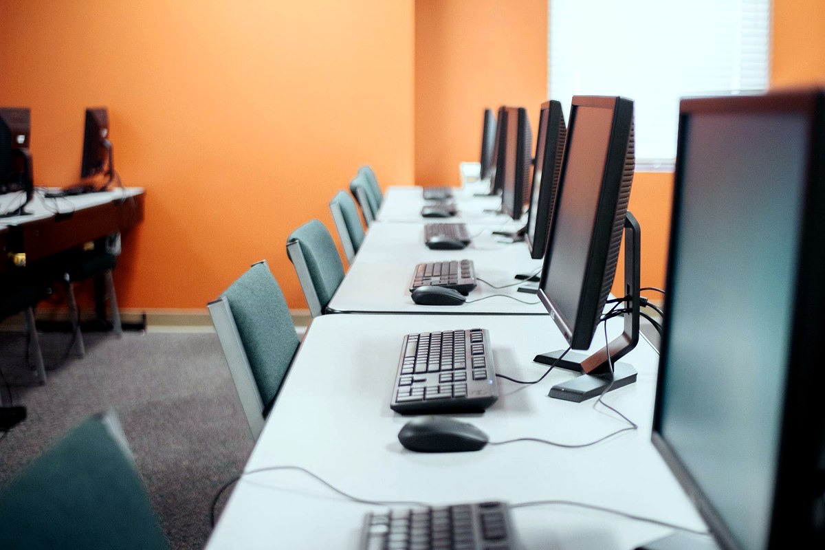 Fila de computadores de escritorio en una sala de cómputo empresarial moderna y bien iluminada, listos para uso corporativo