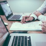 Dos profesionales revisando y firmando las cláusulas de un contrato SLA de soporte TI junto a laptops en una oficina
