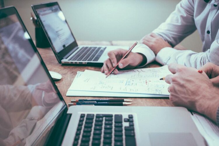 Dos profesionales revisando y firmando las cláusulas de un contrato SLA de soporte TI junto a laptops en una oficina